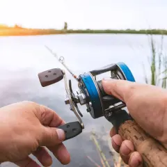 Dłonie trzymające niebiesko-srebrną wędkę spinningową nad wodą.