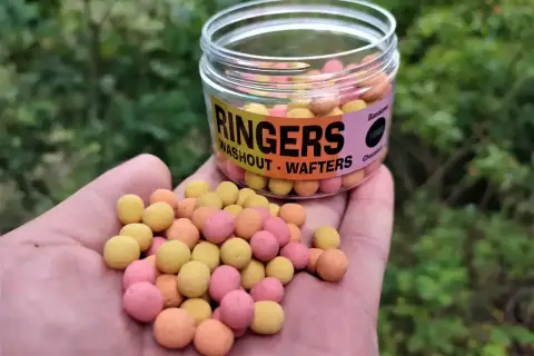 Kolorowe kulki zanętowe Ringers Washout - Wafters w dłoni, obok słoiczka. Idealne na połów.