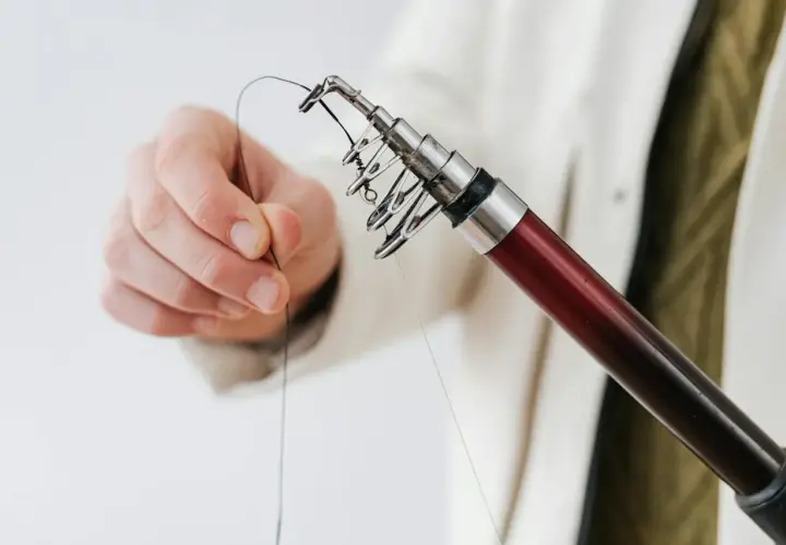 Dłoń przygotowuje żyłkę do zarzucenia, pokazując podstawowe węzły wędkarskie na końcu wędki.